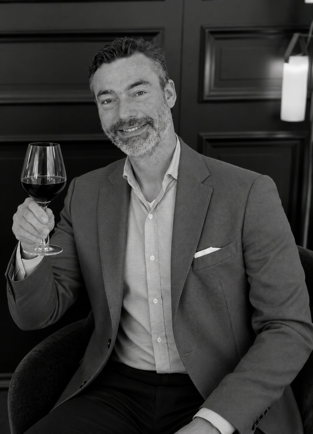 Sander in black and white, smiling and raising a glass of red wine